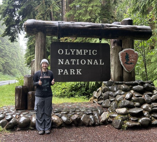 Ashlee standing in front of the sign for Olympic National Park.