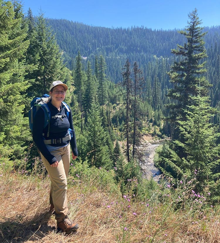 Emma standing on ridge overlooking a river and forest.